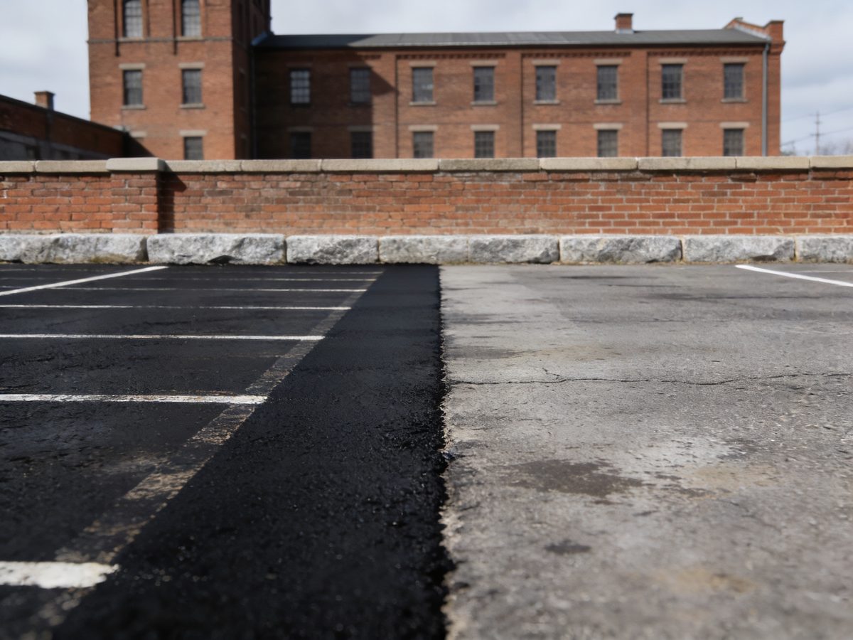 A parking lot with a freshly sealcoated section beside faded grey asphalt